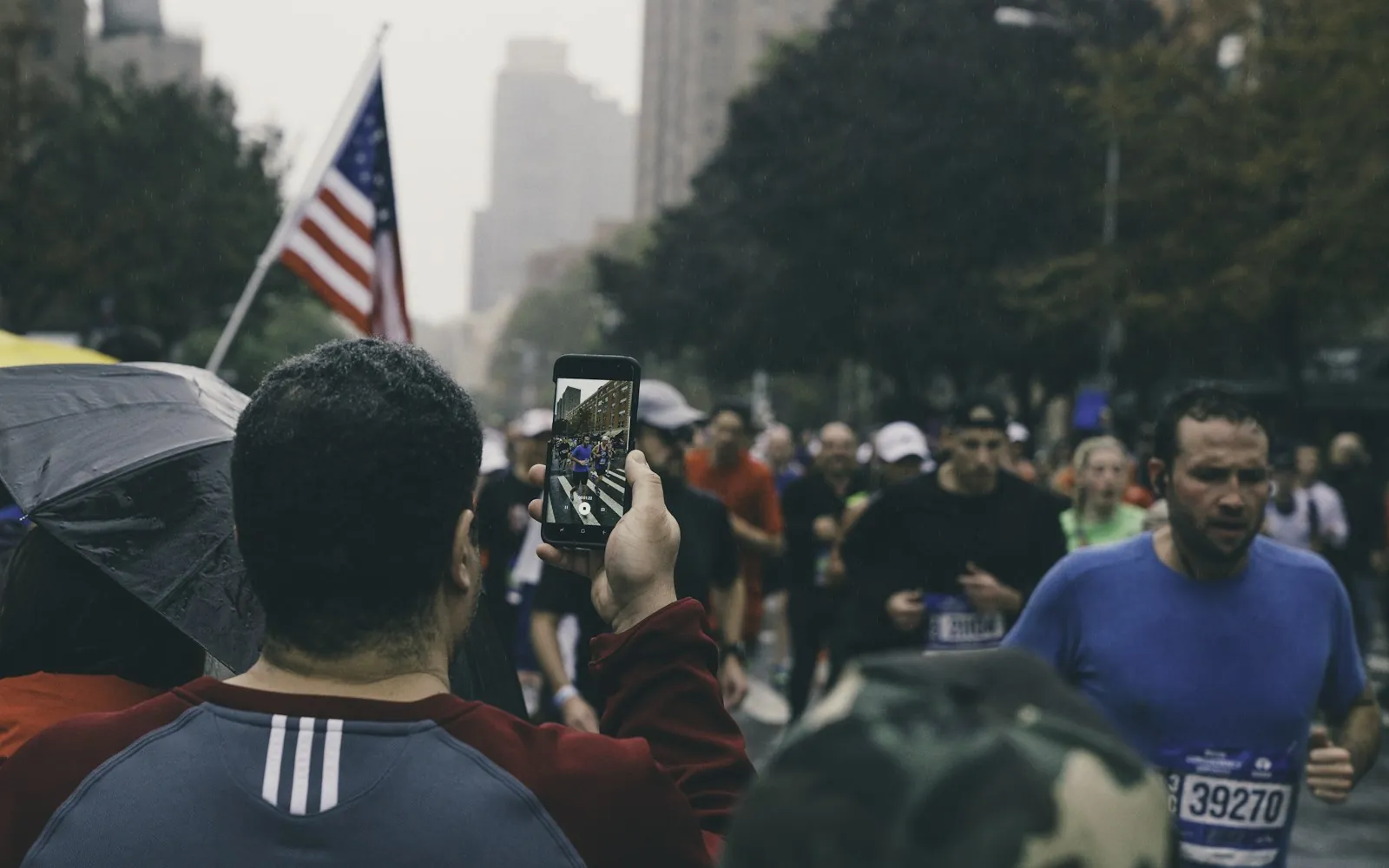 Un espectador graba con el móvil a los corredores que pasan cerca de la esquina noreste de Central Park, en Harlem, en el Maratón de Nueva York de 2017